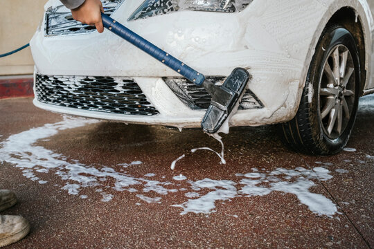 Close-up of car wash brush scrubbing bumper with foam