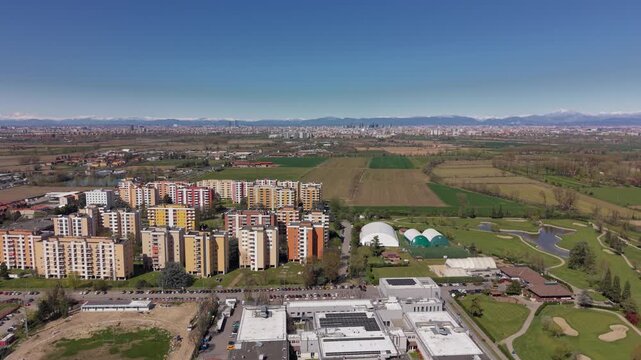 Aerial Cityscape: An eye-level aerial view shows residential apartments, commercial buildings, green spaces, and a clear blue sky, presenting a modern city.