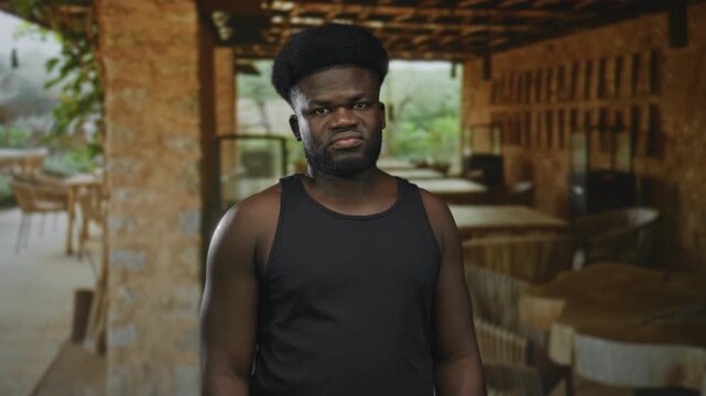 Man with bare shoulder shrugs and grimaces in restaurant building terrace; annoyed resignation fatigue.