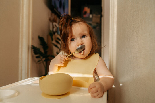 Young girl eating with spoon in bright modern kitchen