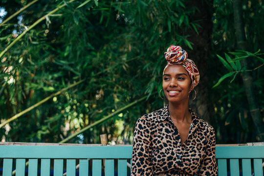Serene woman in head wrap sitting on bench in garden