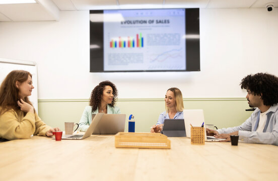 Team meeting in coworking office with sales report screen