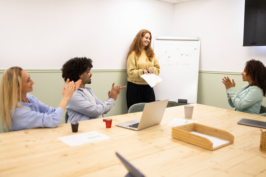 Team applauding coworker presenting in modern office