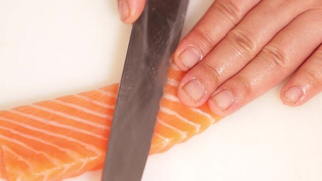 Professional chef slicing fresh salmon fillet for sashimi on white cutting board with sharp knife