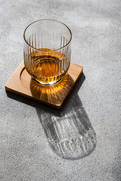 Glass of apple cider on wooden coaster with long shadow