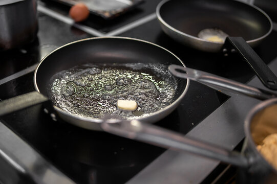 Butter melting and sizzling in a black non-stick frying pan on a modern induction stovetop in a professional kitchen
