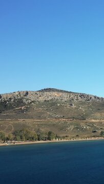 Clear blue sky over a rocky hillside and calm shoreline at Paralia Karathona, near Nafplio, Greece. Tranquil coastal landscape with natural scenery.