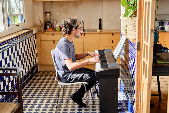 Man of Hispanic descent plays keyboard in home office setting