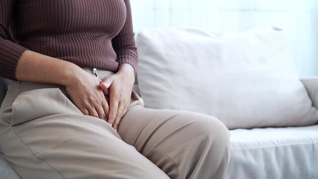 Woman clutching her lower abdomen in pain ,itchy vagina suffering from menstrual cramps, urinary tract infection, or bladder issues at home. Concept of gynecology and female healthcare