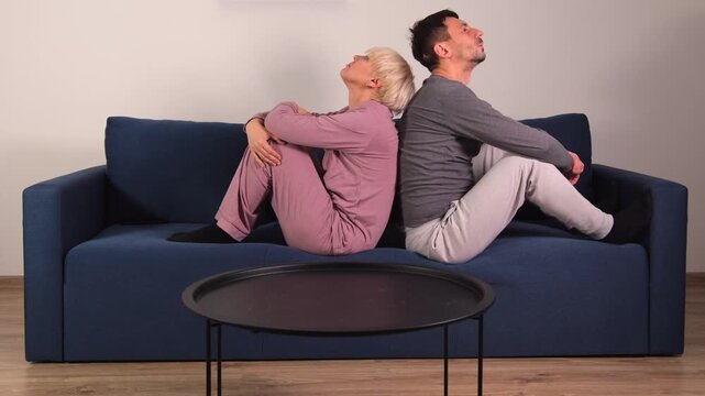 Young couple sitting back to back on a sofa at home, showing tension, disagreement and emotional distance in their relationship. Concept of family problems, conflict, misunderstanding, 