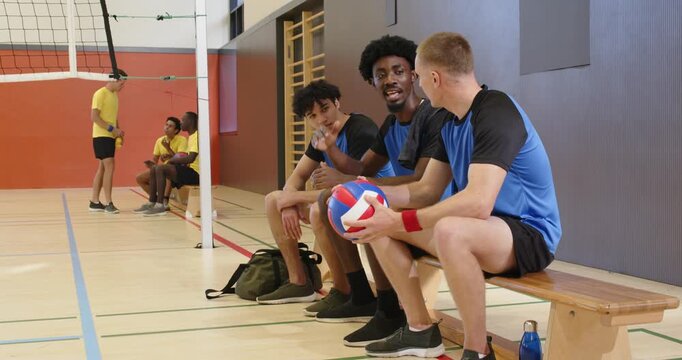 Male blue trio sitting on gym bench at break, holding volleyball, preparing rejoin play, copy space