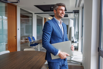 Confident businessman carrying laptop, looking forward with vision in modern office, embracing success and future growth © PeopleVideos