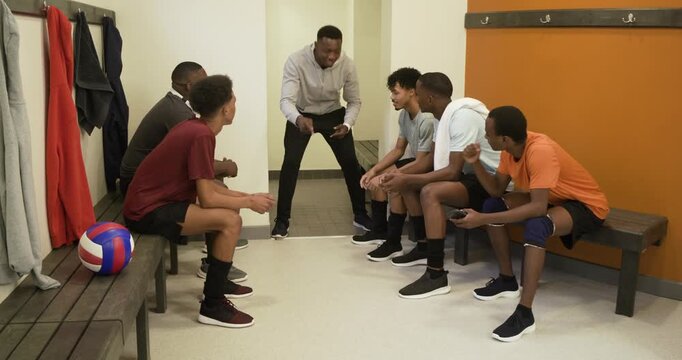 Male team listening to African American coach entering locker-room doorway, giving pep talk pregame