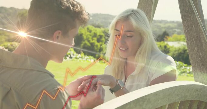 Man bringing woman's hand sliding ring onto finger proposing while tech graphs rising around couple