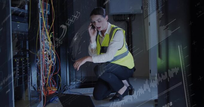 Receiving call female tech kneeling in rack aisle using laptop pointing cables wearing vest fixing