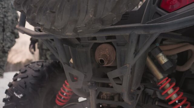 Snowy scene with ATV motorcycle. Closeup of ATV muffler emitting steam. Rear wheel spinning on snowy winter trail background. Rider preparing ATV for ride as exhaust steam disperses over snow