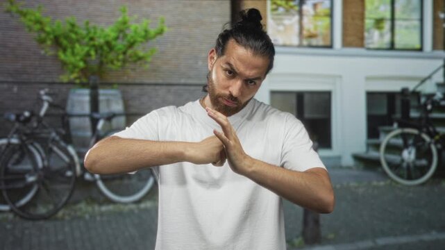 Man with bun and beard cracks knuckles in white t shirt on street in front of building; determination confrontation.