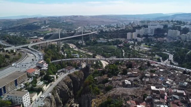 High-angle aerial panorama of the Salah Bey cable-stayed bridge and the urban landscape of Constantine, Algeria, showing modern infrastructure and the Rhumel River gorge.