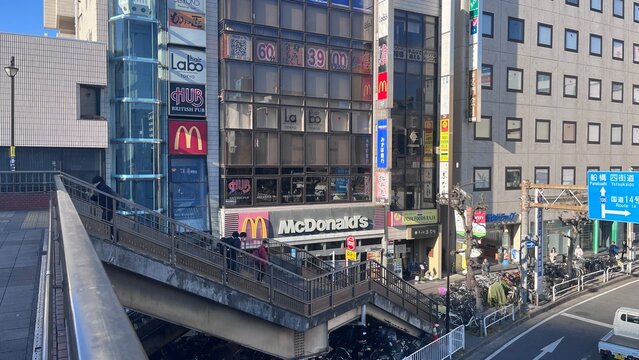 Busy urban street scene in Funabashi with dense vertical signage for McDonald's and HUB British Pub over a pedestrian bridge - Chiba, Japan, December 7, 2025