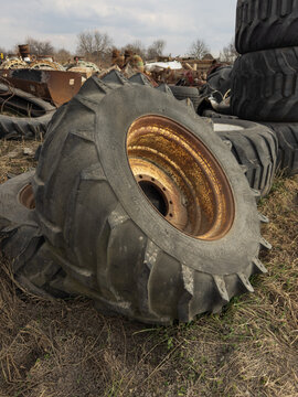 Stack of large used tractor tires and abandoned agricultural machinery in a rural scrapyard. Industrial outdoor scene with worn equipment, rusted metal and countryside background. 
