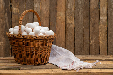 Chicken eggs in large wicker basket with wall of chicken coop, barn or wooden grunge fence in the background. Countryside setting © TSViPhoto