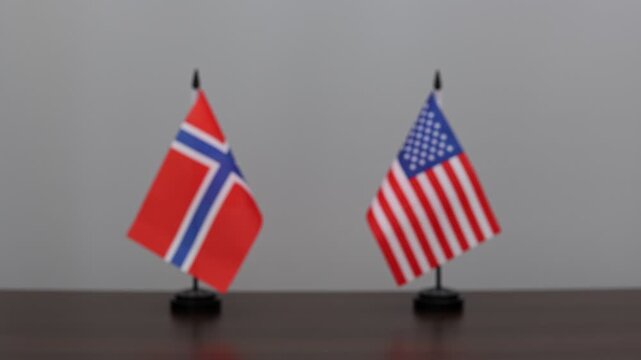 Close up view of a handshake between Norwegian and American businessmen or politicians in a formal setting. Official meeting and agreement with national flags of Norway and USA on background.
