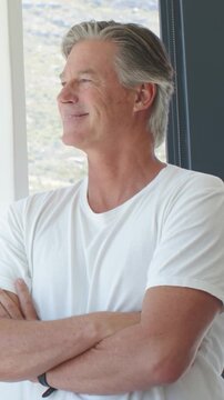 Vertical video: Standing mature man greeting sun, gazing, smiling at window, wearing white tee