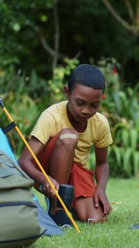 Vertical video: Hammering boy in yellow tee on lawn, placing stake, securing tent, giving high five