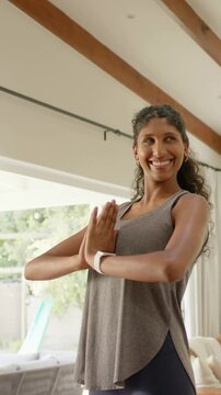 Vertical video: Sunlight drawing woman holding prayer pose at home, wearing tank top, fitness watch