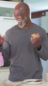 Vertical video: Bringing toast forward, man in henley laughing, eating in kitchen reacting to hand