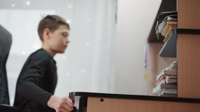 Teen reaching across desk for pen, focused student grasps marker and adjusts notebook, steady posture in ergonomic chair, soft curtain light, intentional and driven study moment in bedroom