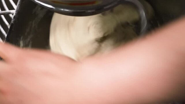 High-definition footage capturing a close-up view of dough being mechanically kneaded inside a stainless steel, commercial-grade bakery mixer using a dough hook attachment.