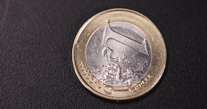 one coin of the European Union with a face value of one euro, metal money worth one euro made of combined metals, A coin is spinning in a circle on a black rotating platform, real currency
