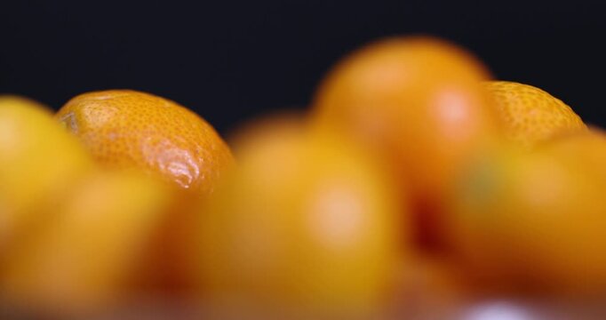 small orange fruits of juicy fresh kumquat on a black wooden table, oval oblong kumquat fruit scattered on a black table made of pine wood