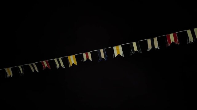 Nautical signal flags on a rope swaying in the night wind for maritime communication, celebration, or decoration against a dark background with copy space