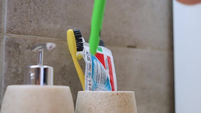 Toothbrushes and toothpaste in holder, closeup of two colorful brushes and squeezed paste tube beside soap dispenser on tiled bathroom wall, bright morning light, minimalist family routine, clean