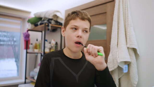 Focused white grandson brushing teeth at sink, closeup mirror angles show concentrated teen expression, detailed mint foam and paste, towel and window in background, intimate grooming scene in family