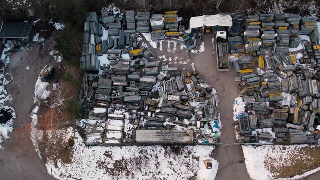 Top down drone view of an outdoor scaffolding storage yard in winter with stacked construction materials, snowy ground and organized industrial inventory in an open work area.