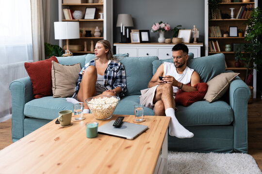 Young couple experiencing jealousy while texting, woman focused on smartphone as boyfriend watches with suspicion and emotional distance