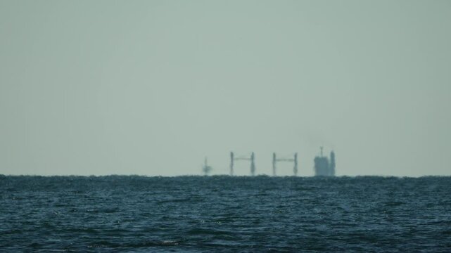 Mirage oil rig sea visible on the horizon as a result of atmospheric refraction over the choppy ocean water