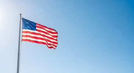 Obraz premium American flag proudly waving against a clear blue sky on a bright and sunny day.