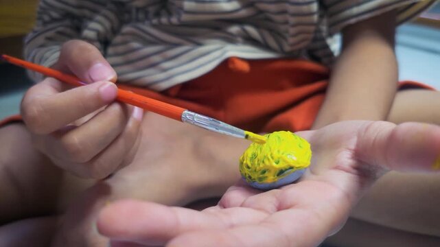Close up shot of a kit painted a stone with yellow color with paint brush. painting activity