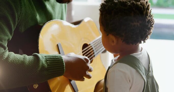 Animation of light flashing over african american father and son playing guitar