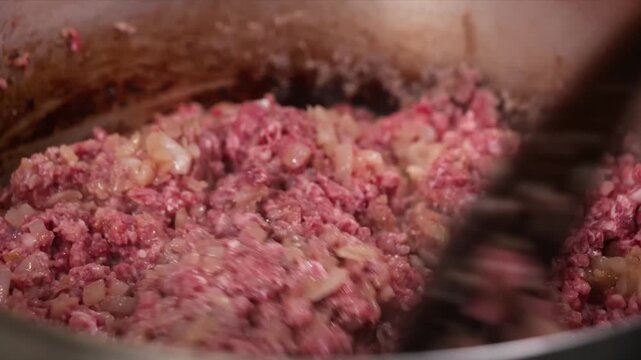 A close-up, static shot of raw minced beef and finely chopped onions being cooked in a pan and stirred with a wooden spatula.