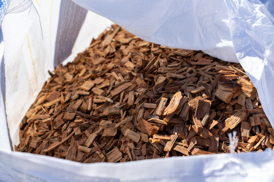 Brown wood chips mulch in large white bulk bag close-up view outdoors in sunlight