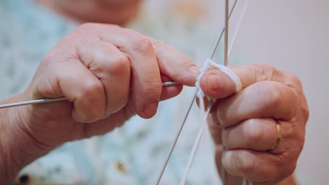 Graceful elderly female delicately crafting stitches with precise movements. Mature Caucasian grandmother carefully manipulating multiple needles to produce intricate knitted patterns