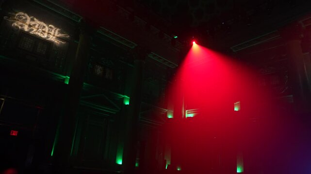 Bright red spotlights cut through the dark atmosphere of an empty stage or venue. The dynamic beams create circular patterns on the floor, evoking an energetic mood for a concert or live event.
