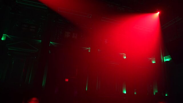 Bright red spotlights cut through the dark atmosphere of an empty stage or venue. The dynamic beams create circular patterns on the floor, evoking an energetic mood for a concert or live event.
