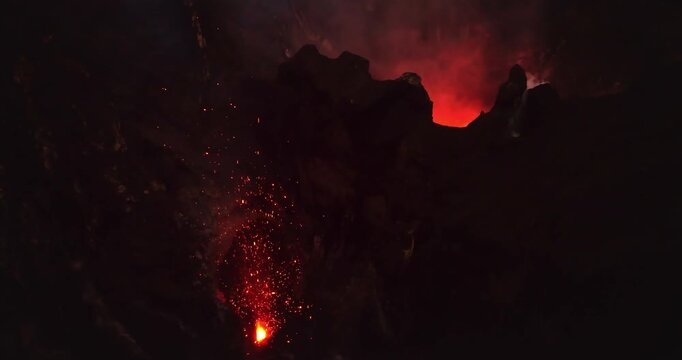 Aerial view of Mount Yasur volcano crater actively erupting, shooting incandescent lava fragments and sparks into the dark night sky, illuminating the rugged volcanic landscape with red glow and smoke