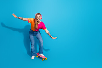 Obraz premium Young girl skateboarding in a colorful t shirt and pink headphones smiles against a bright blue background for lifestyle fashion promotion